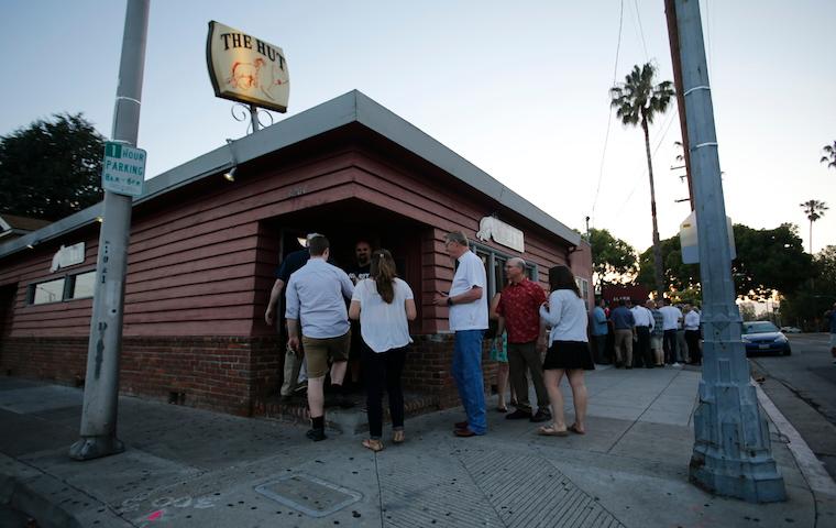 People standing outside a brick building titled The Hut. image link to story