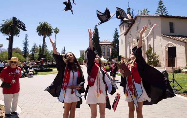 Three female graduates toss their caps in the air alongside Mission Church