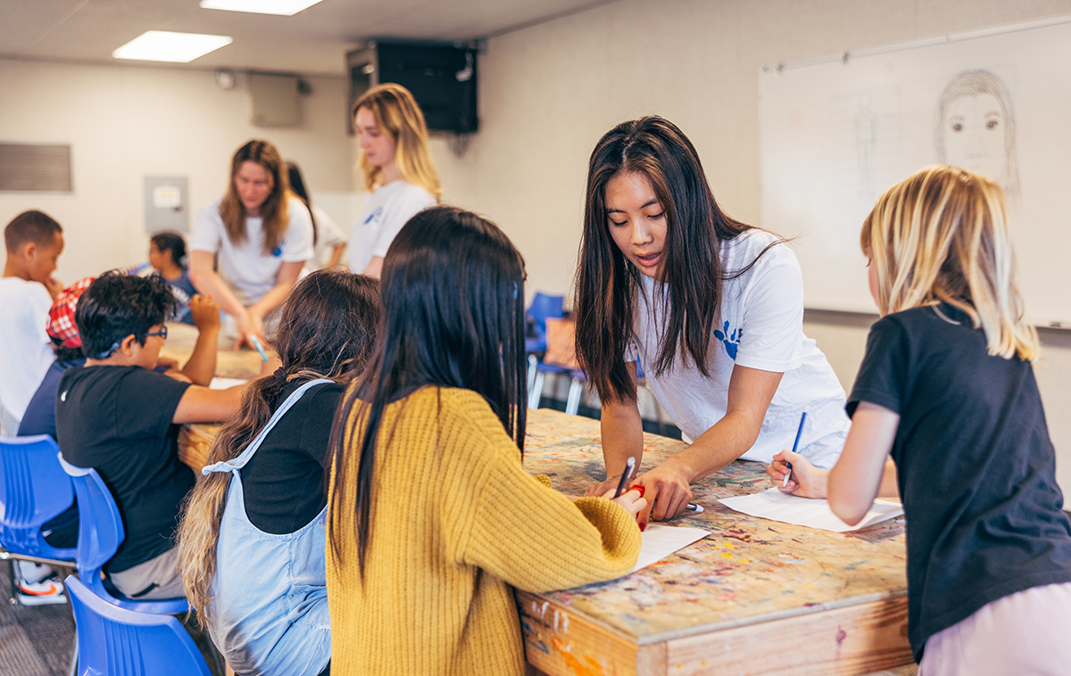 Megan Baldemor works with kids on arts project on table in classroom