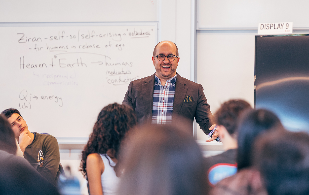 Paul Schutz teaaching in classroom in front of white board with students seated in foreground.