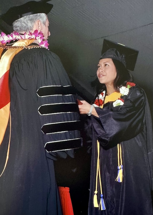 Amielynn Abellera in a cap and gown accepts a diploma.