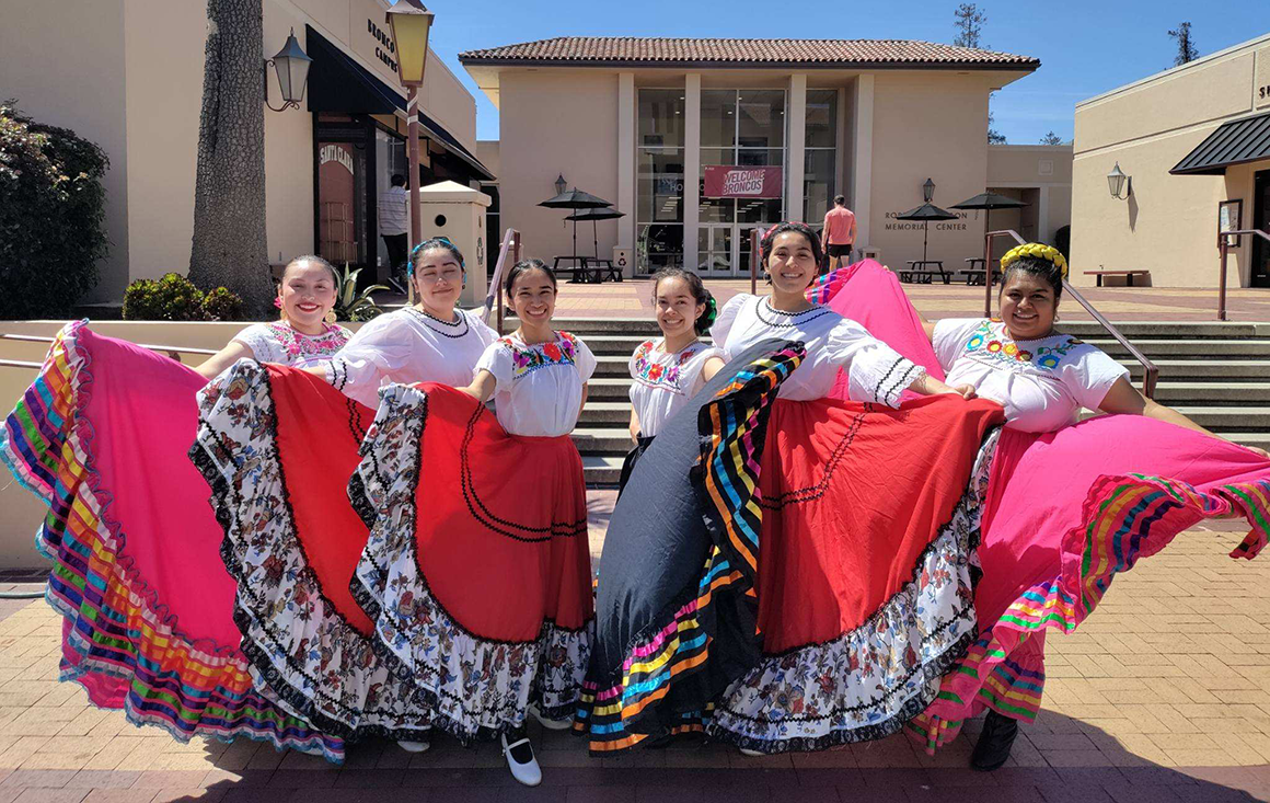 A group of students in colorful Mexican folk dresses - some with ribbons, some with floral patterns.