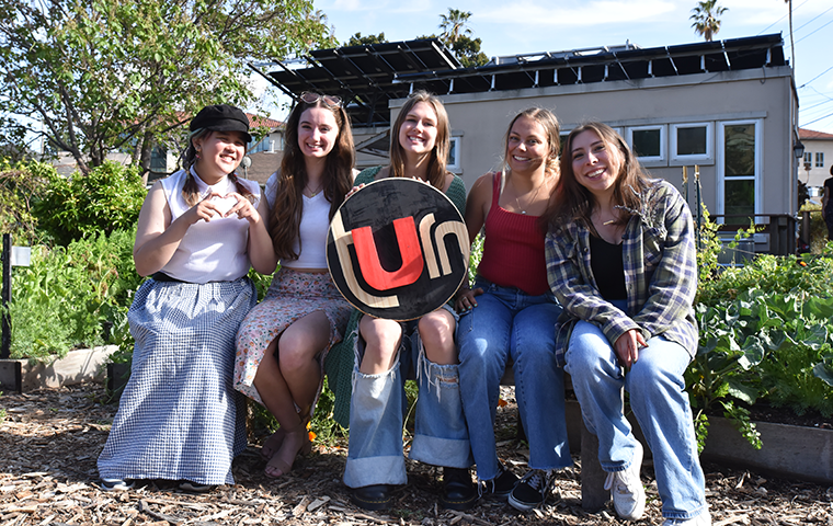A group of students sitting in a garden holding a circular sign saying 
