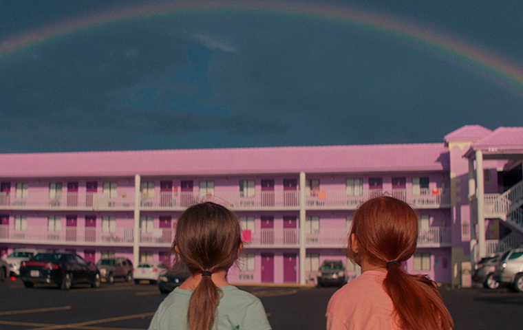 Two girls stare at rainbow over a pink motel.