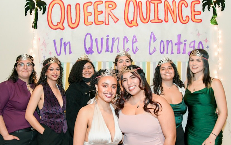 A group of women in formal wear and crowns stand under a banner saying 