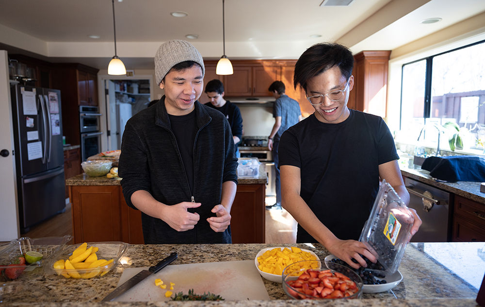 Two students prepare food in a kitchen, side by side.