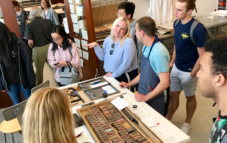 A group of students gather and talk around a table of letterpress types.