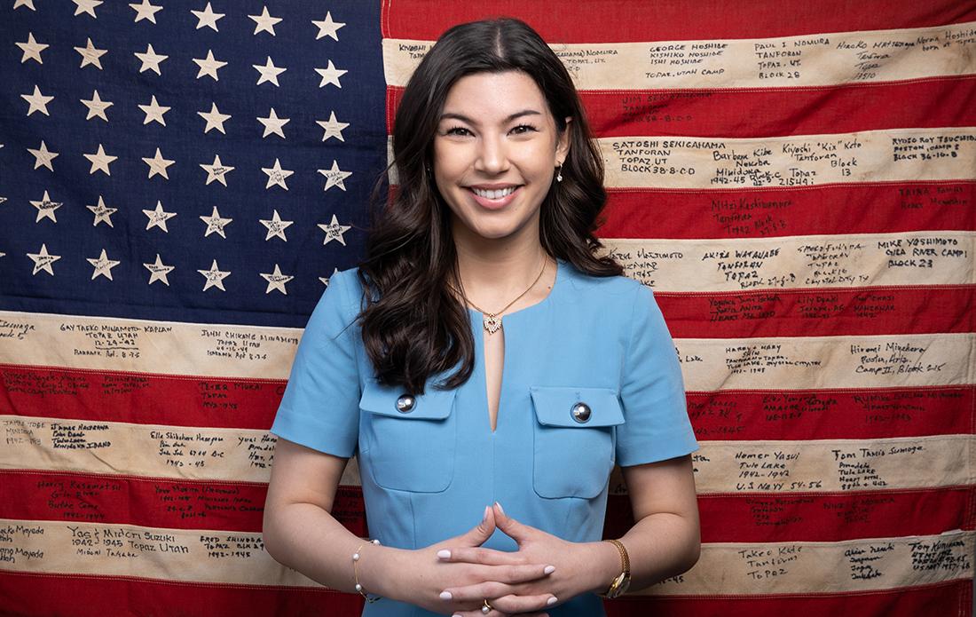 Jordan Tachibana 23 stands before a 1948 U.S. flag inscribed with signatures of Japanese Americans incarcerated in internment camps.