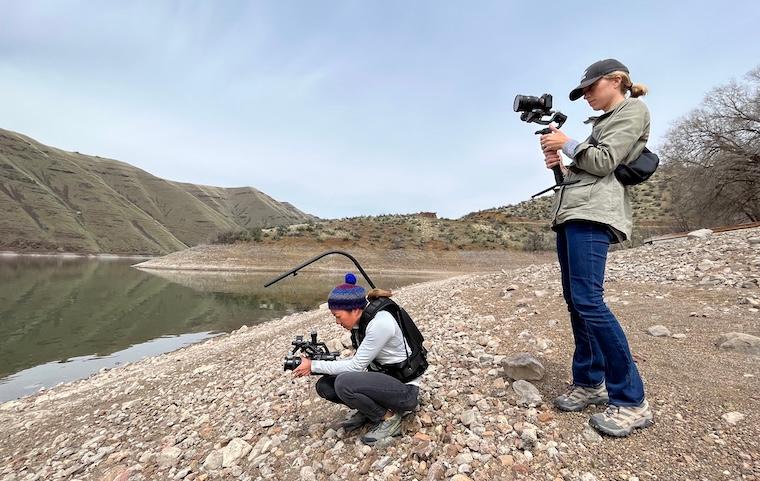 Two women with cameras film footage on the bank of the Snake River in Idaho.