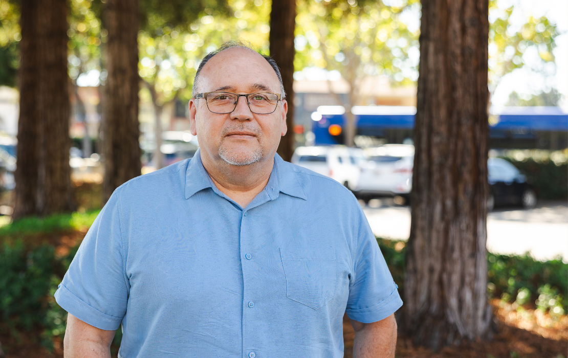 Professor Marco Bravo standing in front of trees and passing cars