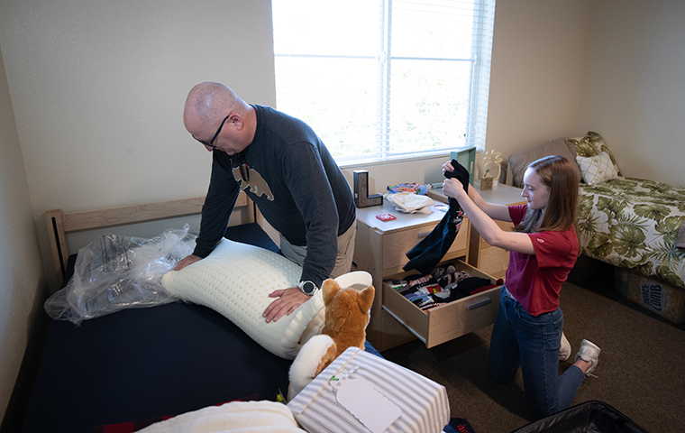 Father and daughter unpack suitcases into residence hall room