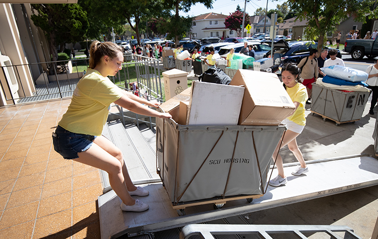Two students move a dolly full of items for move-in