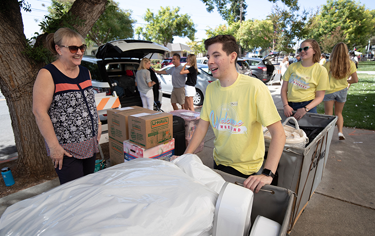 Student pushes dolly of items into residence hall during move-in