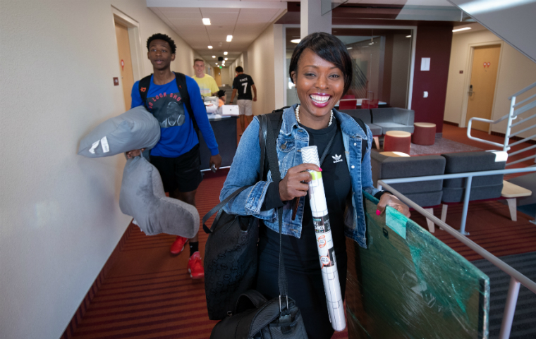Two students smiling holding belongings as they move into Finn Hall