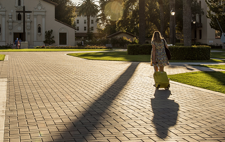 Woman walking into the sunset in front of the Mission with a pull suitcase image link to story