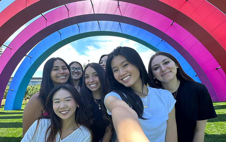 A group of young women pose for a selfie under a colorful series of archways.