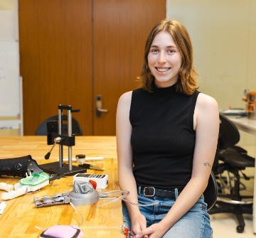 A female student seated in the DART Lab with a prosthetetic hand prototype.