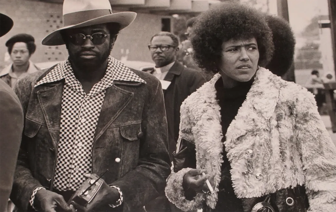 Historical photo (1974) of Elaine Brown (right) wearing a coat walking next to a man