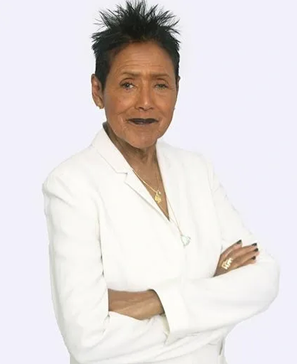 Elaine Brown standing with her arms crossed in a white suit