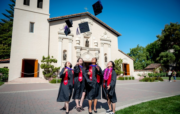 Four women law graduates throwing hats in the air in front of the Mission