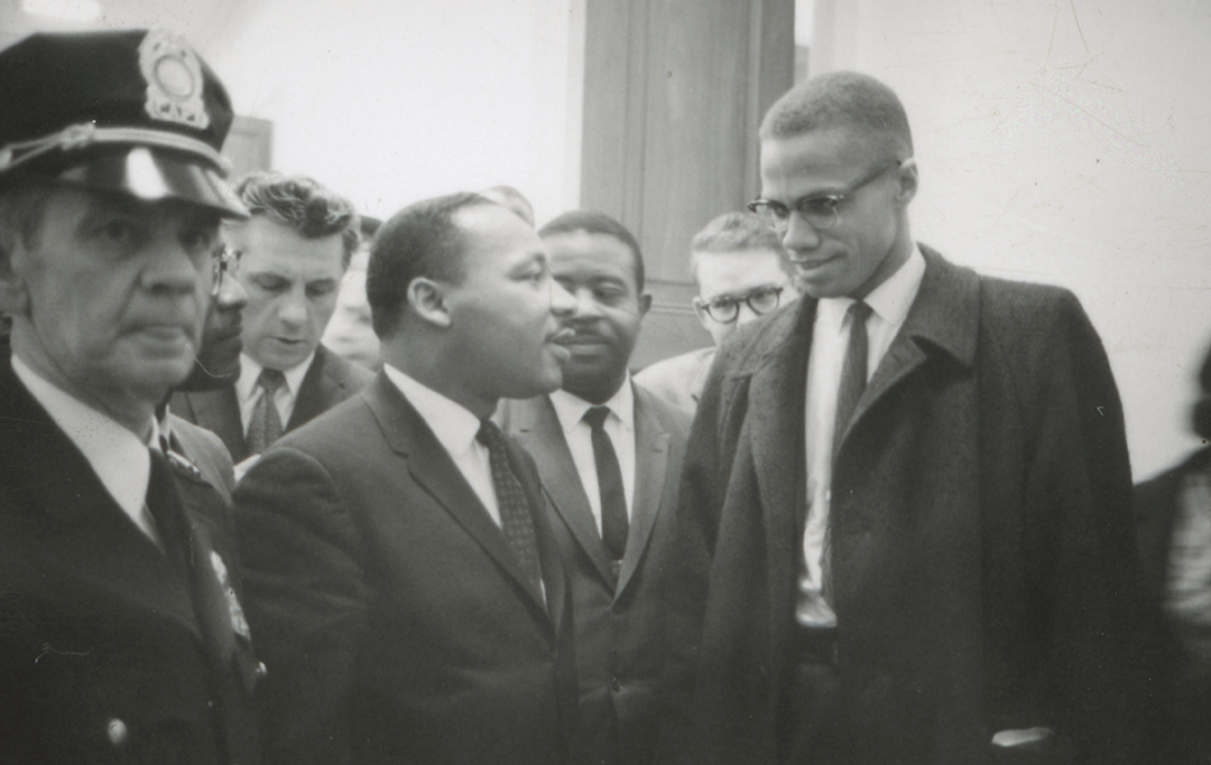 Martin Luther King and Malcolm X shake hands in a crowded room