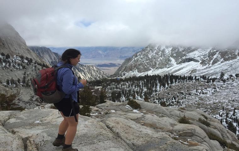 A person hiking on a mountain trail with snow-covered peaks in the background. image link to story