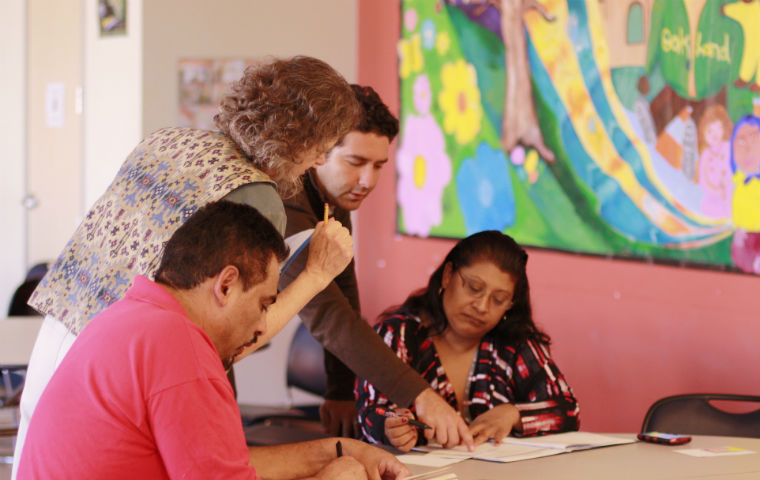 Four people looking at papers on a table, in front of colorful art. 