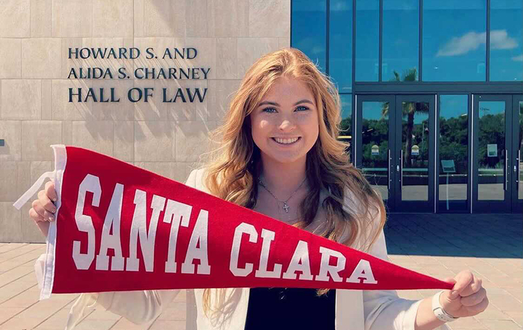 Tawni Henderson holds a SCU pennant, standing in front of the Charney Hall of Law