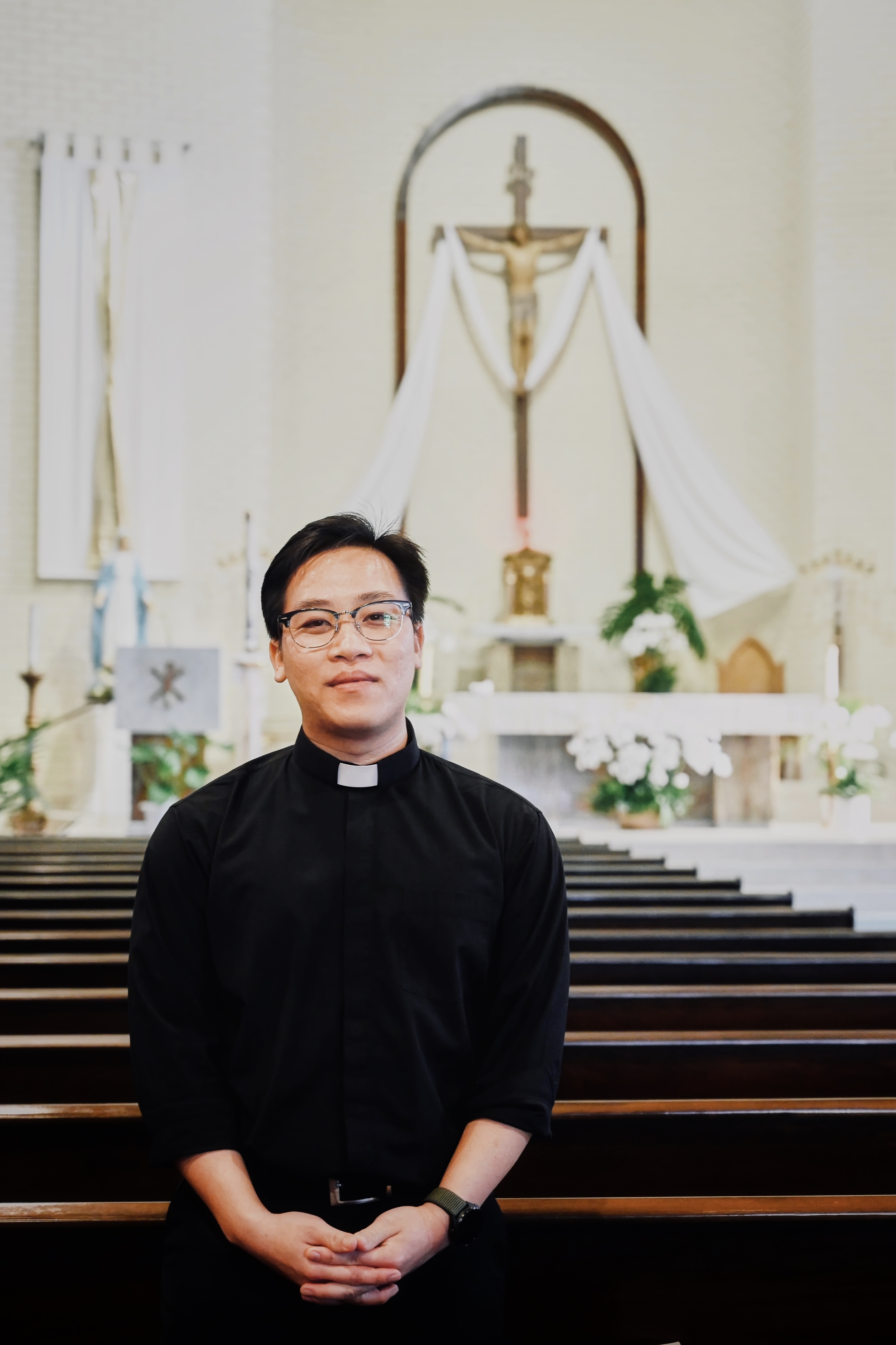 A man in a clerical collar standing in a church with pews and an altar in the background