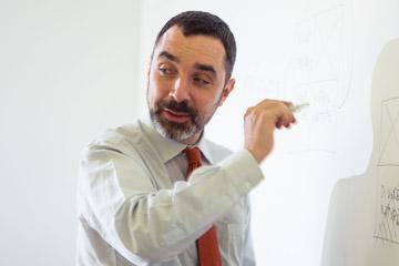 A professor writes on a white board  
