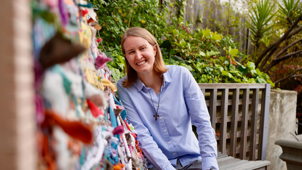 A woman smiling. She is next to a piece of abstract art, which the camera line follows from the foreground to the subject.
