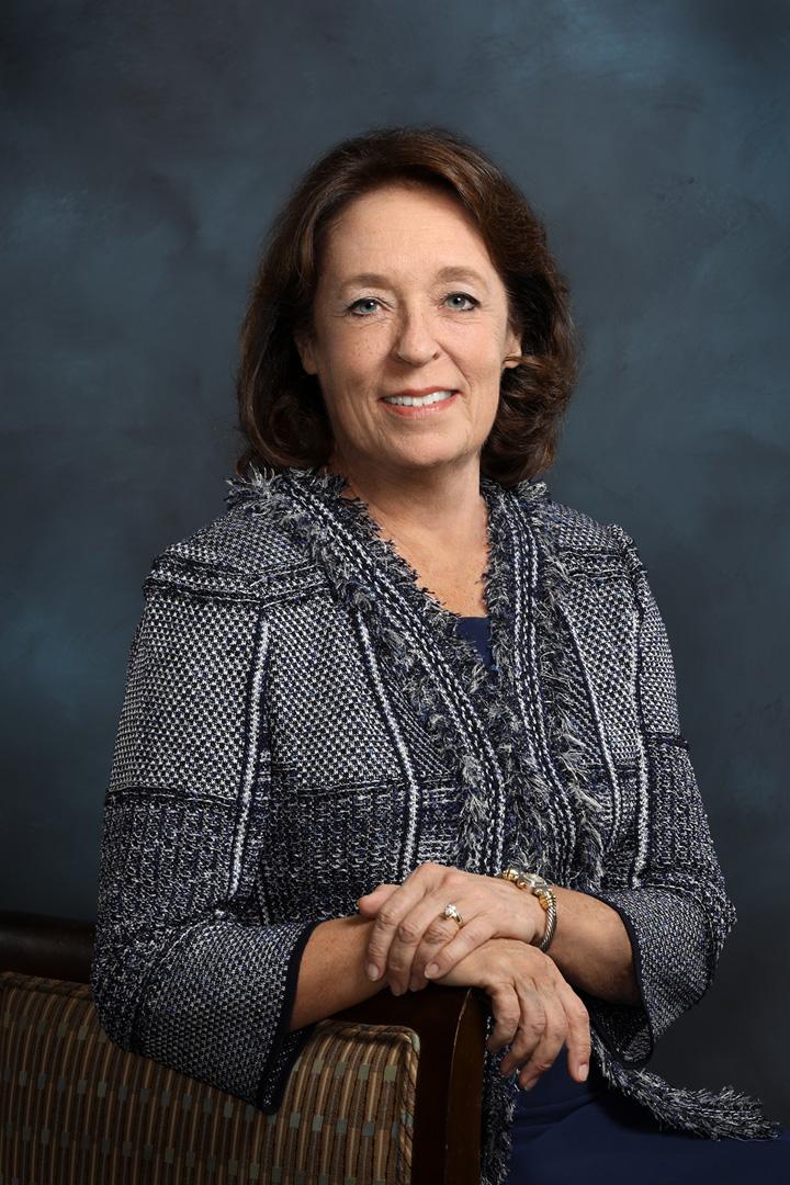 A woman smiles in front of a grey background
