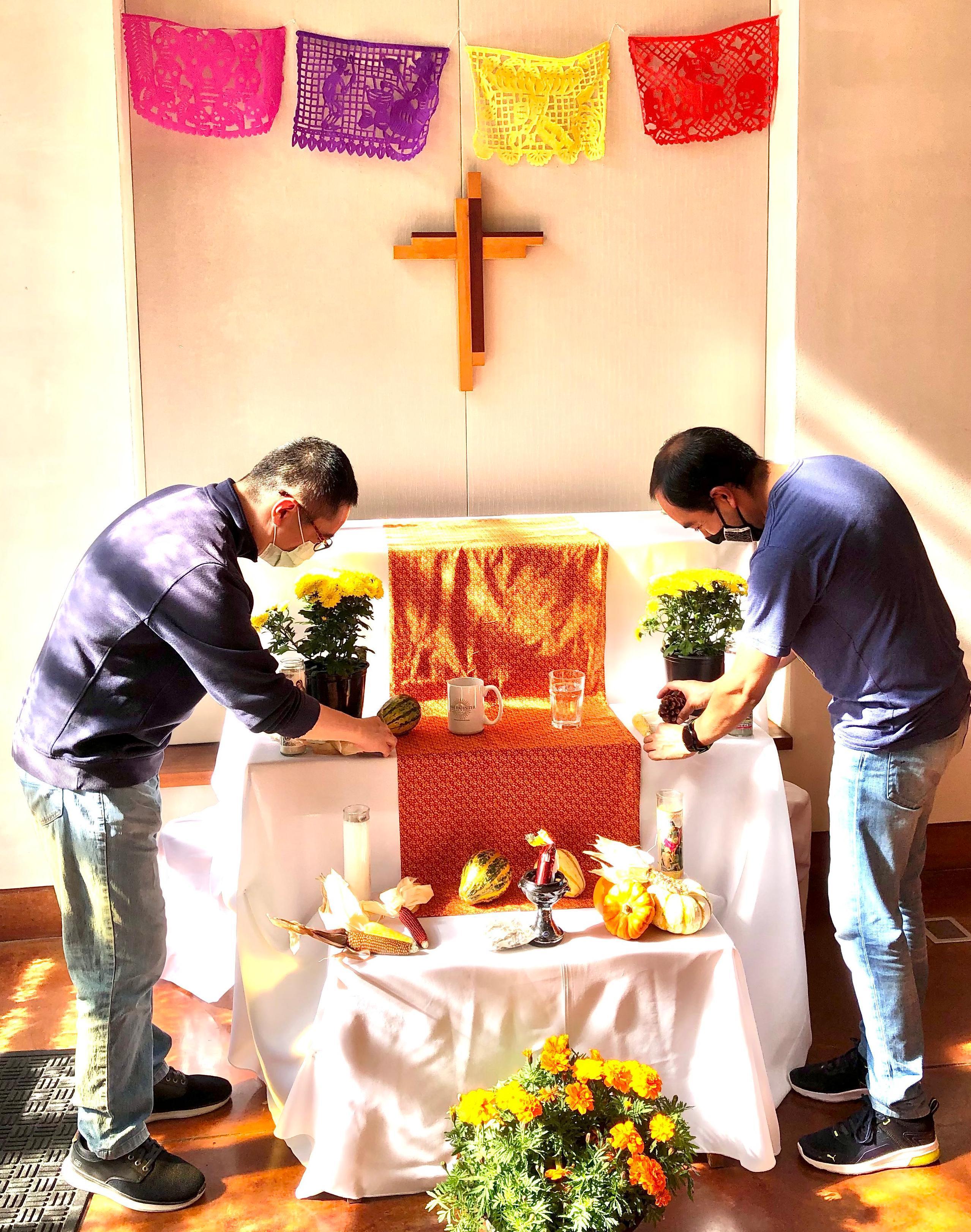 Two people setting up an altar with decorations and flowers.