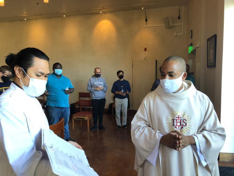 Two people in ceremonial clothing and masks in front of a group.