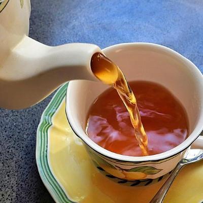 A teapot pours tea into a cup on a saucer with a spoon.