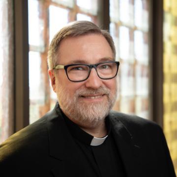 A person with glasses smiling in an indoor setting.