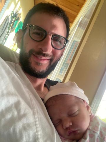 James smiling with his sleeping newborn