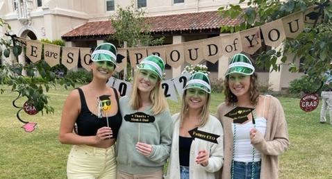Four people celebrating graduation outdoors with diploma covers and caps.
