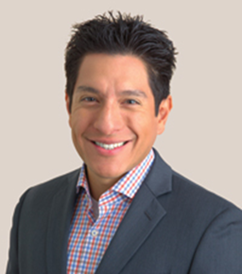 A man in a suit smiling against a beige background.