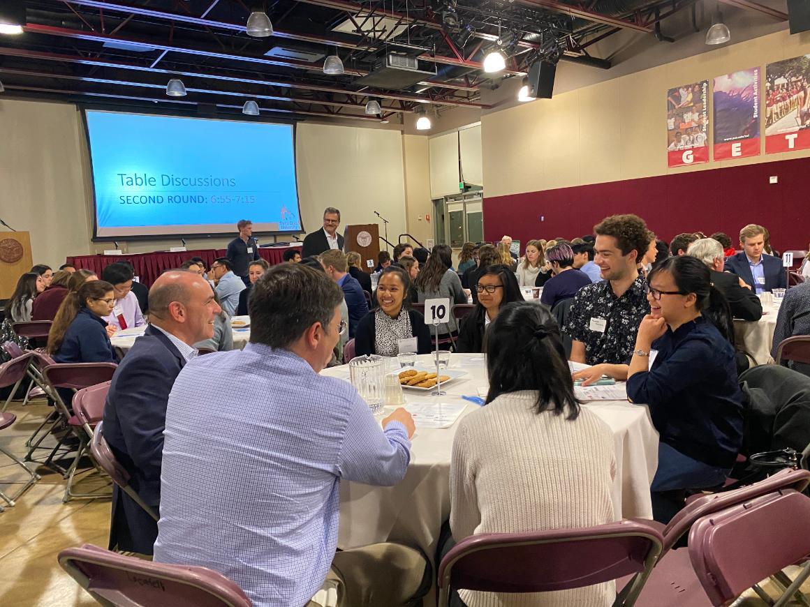 Attendees gathered around tables during ACTG Info Night, with a presentation in the background.