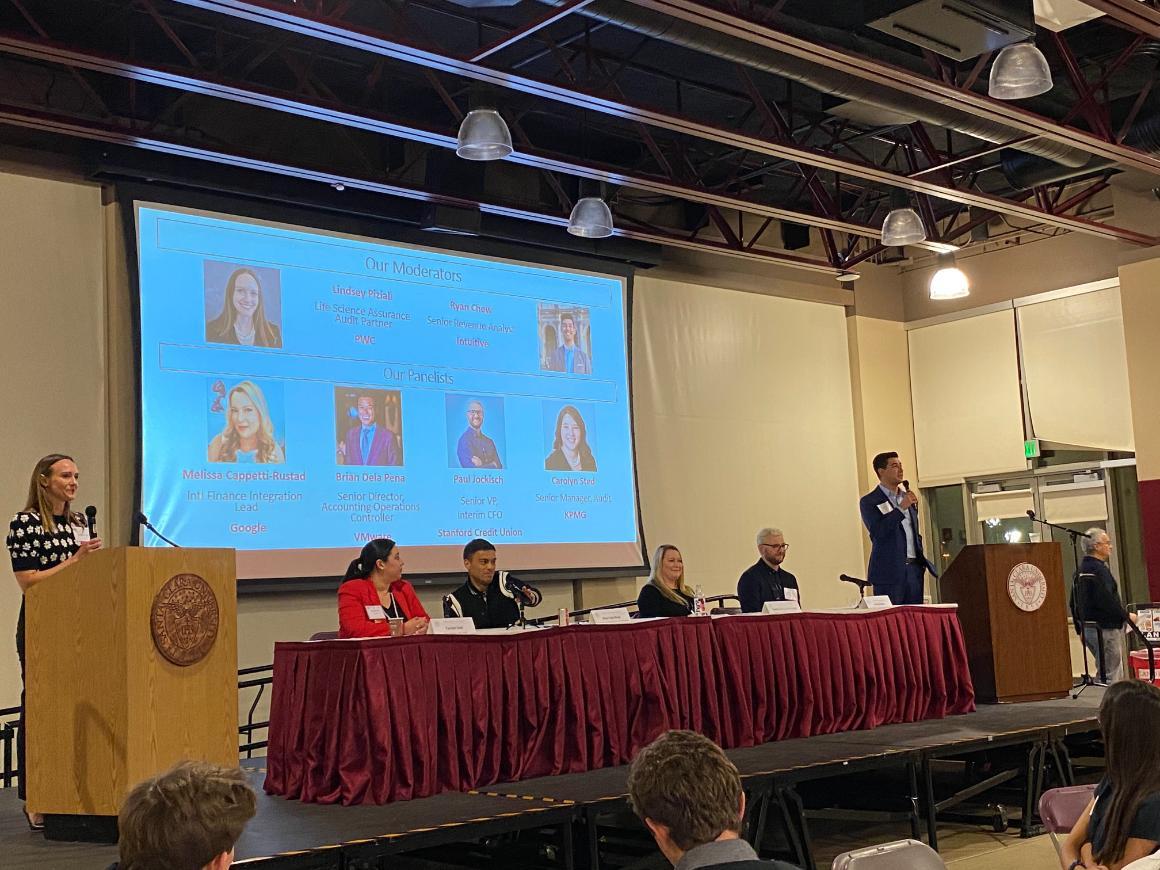A panel of six people seated in front of a screen.