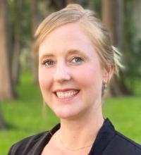 A person smiling outdoors with trees in the background.