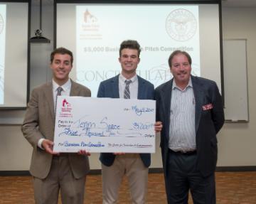 Three individuals holding a large check in a classroom setting.