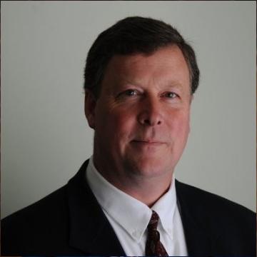 A man in a suit and tie against a neutral background.