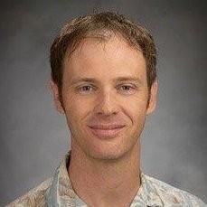 A man wearing a patterned shirt against a gray background.
