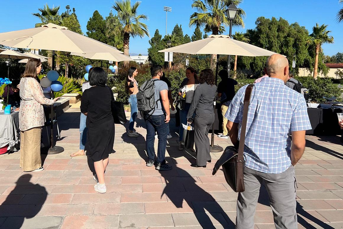 People socializing at Ciocca Center Beach Day event with sun umbrellas in the background.