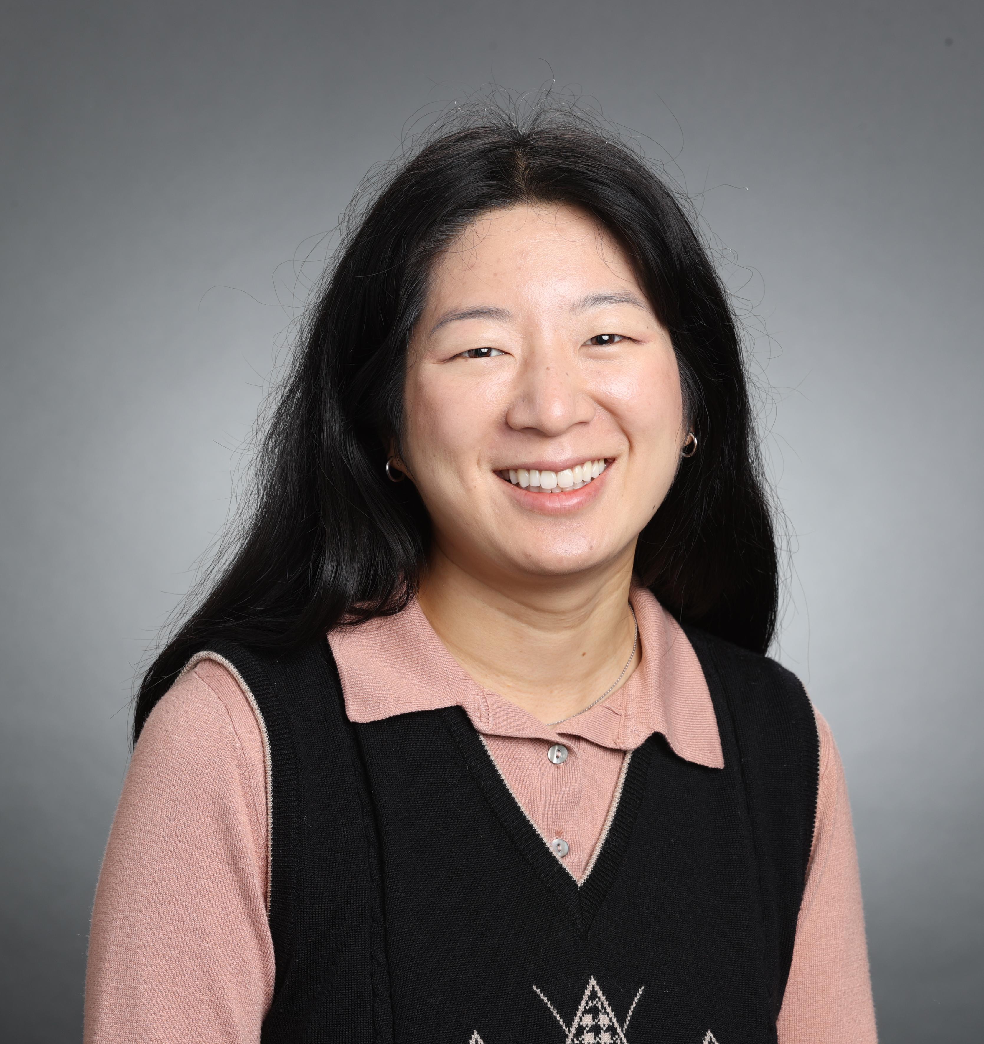 A person smiling in front of a gray background.