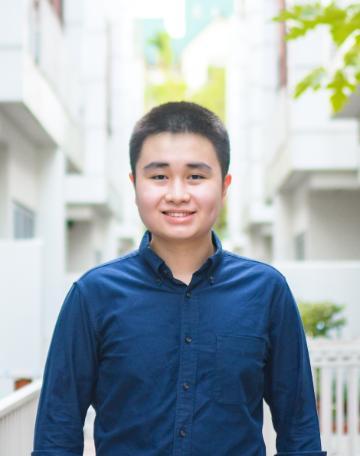 A person smiling and standing in an urban outdoor setting.