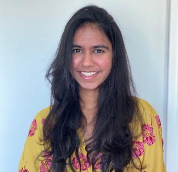 A person smiling, wearing a yellow floral top with long hair.