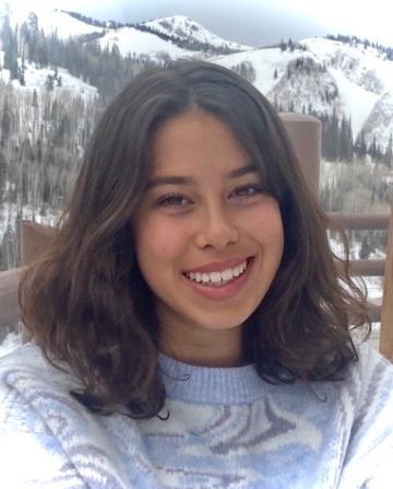Smiling person in winter clothes with snowy mountain in the background.